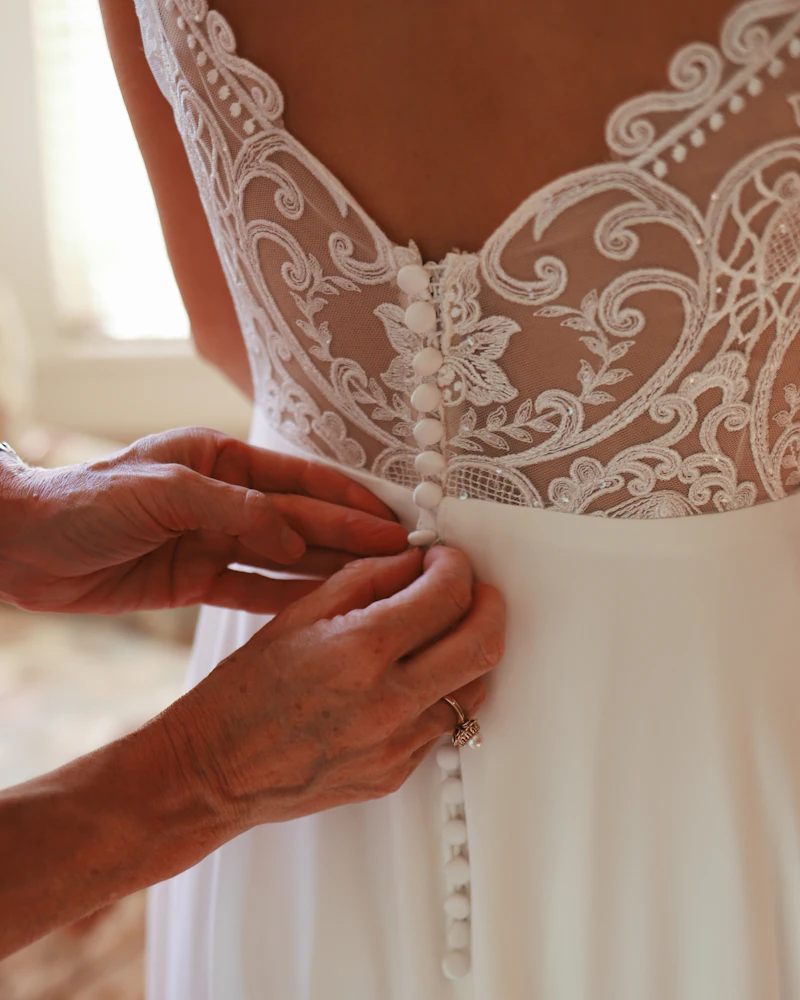 Hands buttoning the back of a wedding dress