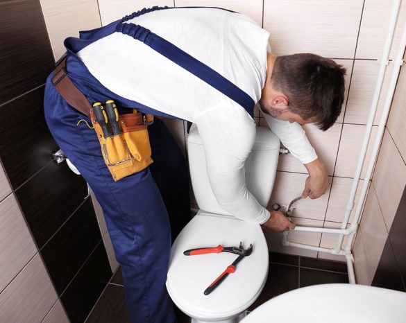 Plumber fixing water hose on toilet
